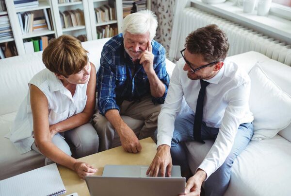 Flexible Spending Account - Senior Couple Planning Their Investments with a Financial Advisor from the Comfort of Their Home While Sitting on the Sofa of Their Living Room