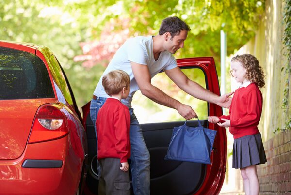 Personal Insurance - Father Hands His Daughter Her Bag as He Drops His Two Kids to School